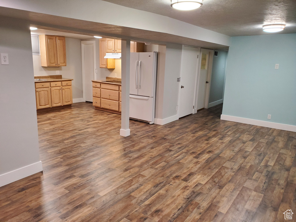 Finished below grade area with freestanding refrigerator, dark wood-style flooring, baseboards, and a textured ceiling
