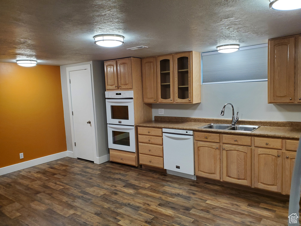 Kitchen featuring white appliances, a sink, a textured ceiling, glass insert cabinets, and dark wood finished floors