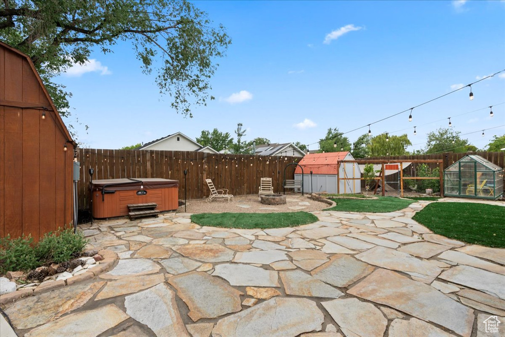 View of patio with a fenced backyard, a hot tub, an outbuilding, a greenhouse, and a storage shed