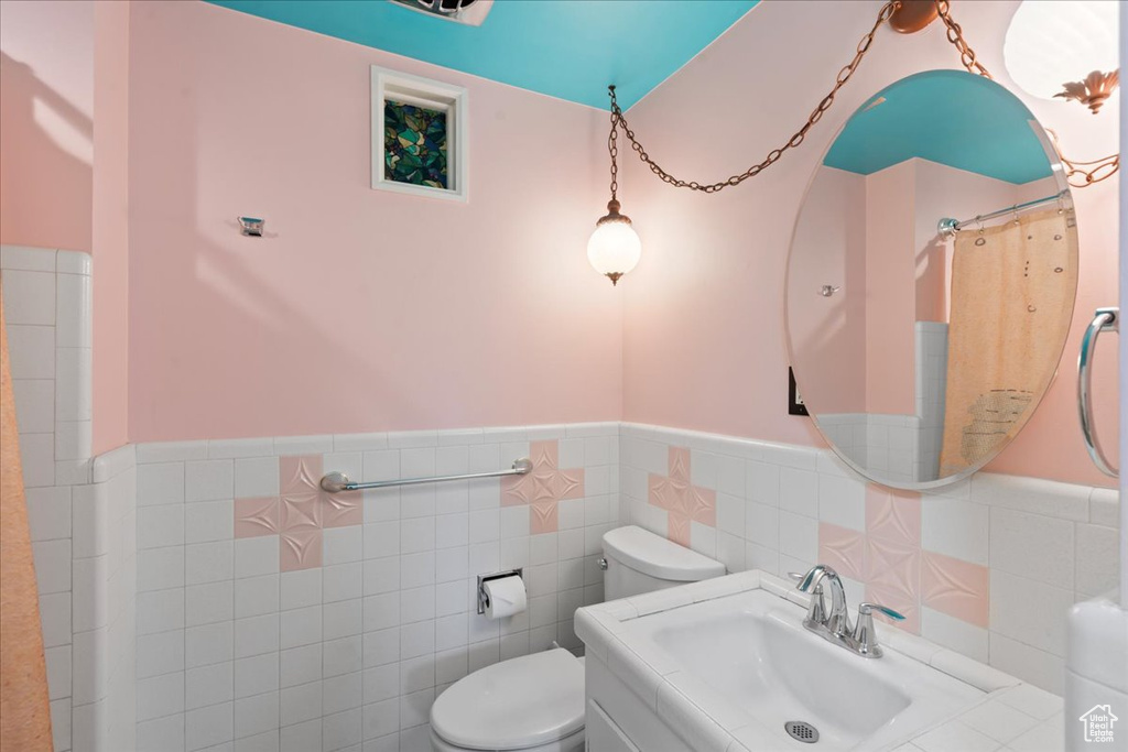 Full bathroom featuring a sink, a wainscoted wall, toilet, and tile walls