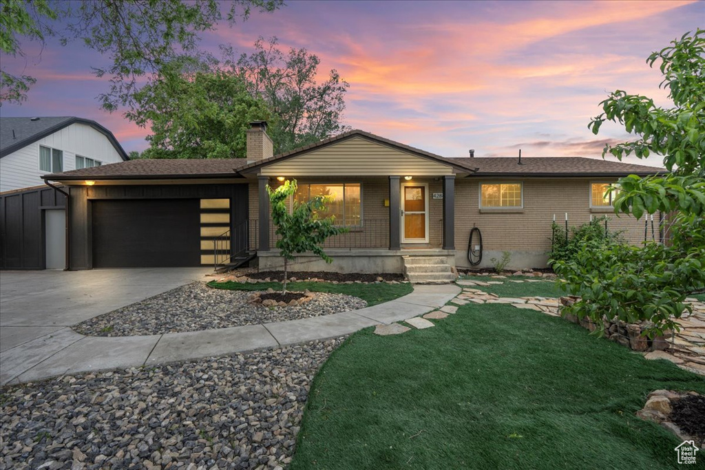 View of front of property featuring an attached garage, a chimney, concrete driveway, a front lawn, and brick siding