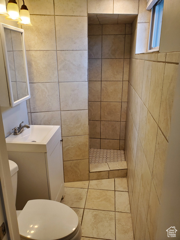Bathroom with toilet, a sink, a tile shower, and tile walls