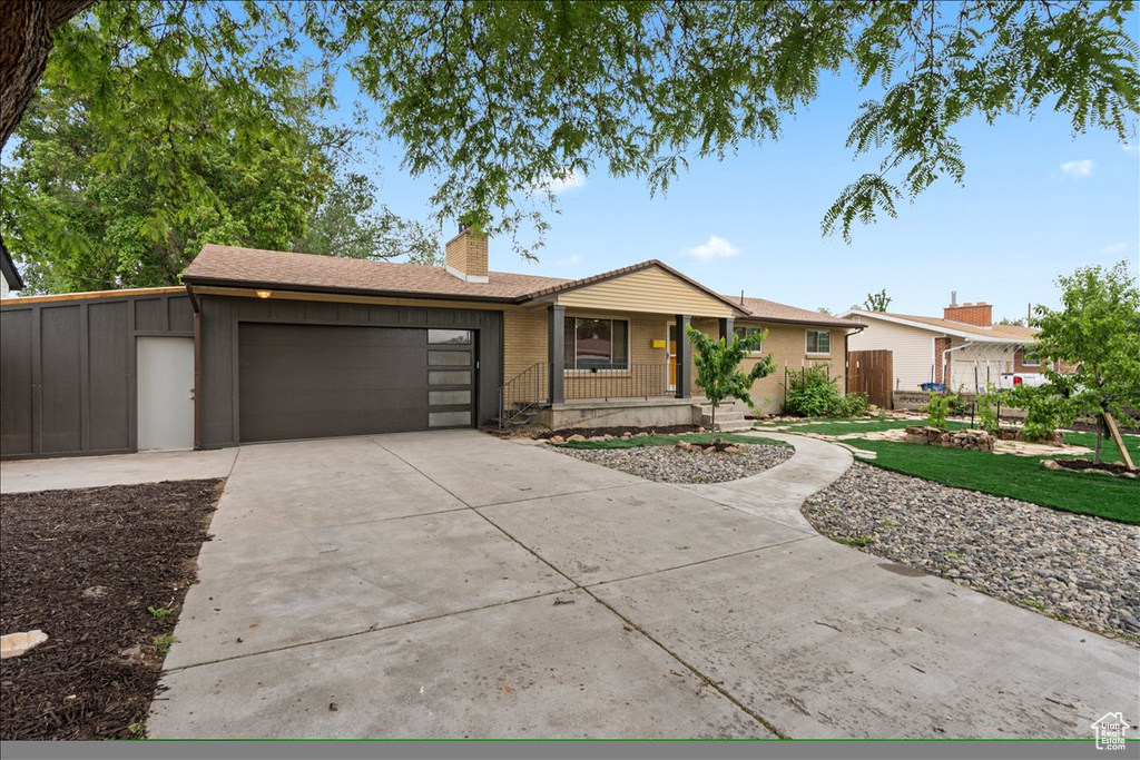 Single story home featuring covered porch, a chimney, an attached garage, concrete driveway, and a shingled roof