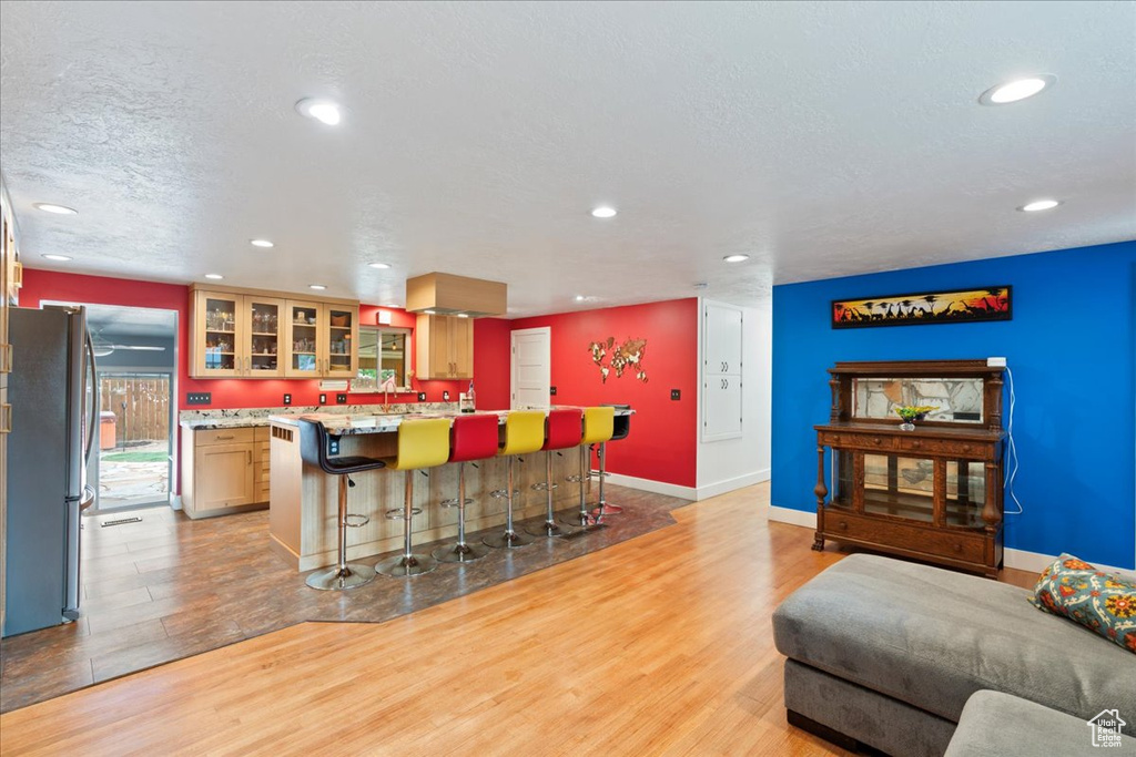 Kitchen with freestanding refrigerator, light wood finished floors, a breakfast bar area, recessed lighting, and glass insert cabinets