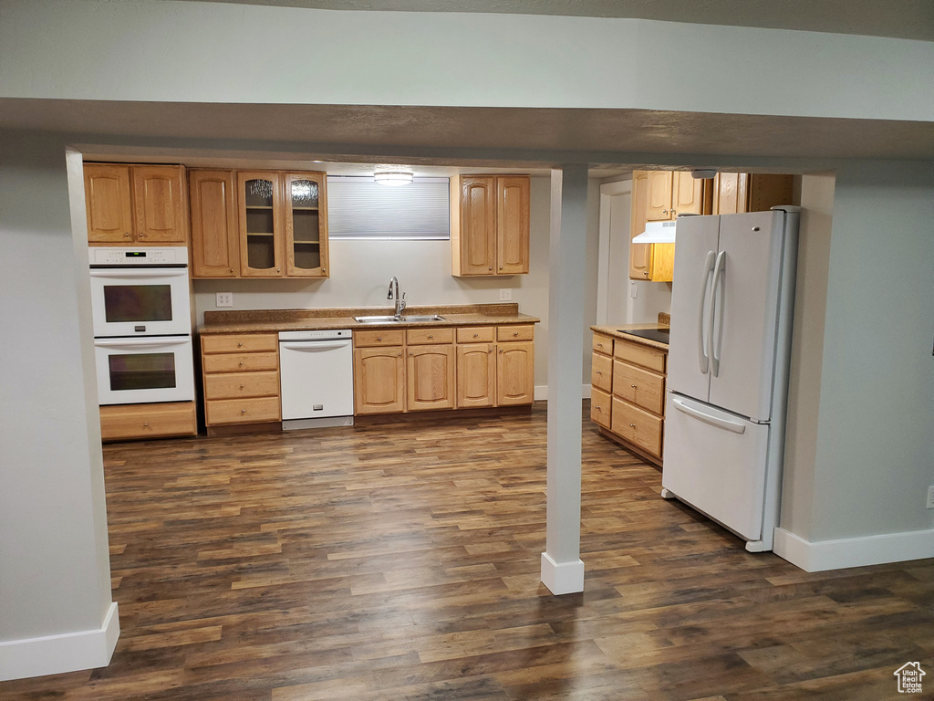 Kitchen with white appliances, a sink, baseboards, under cabinet range hood, and dark wood-style flooring