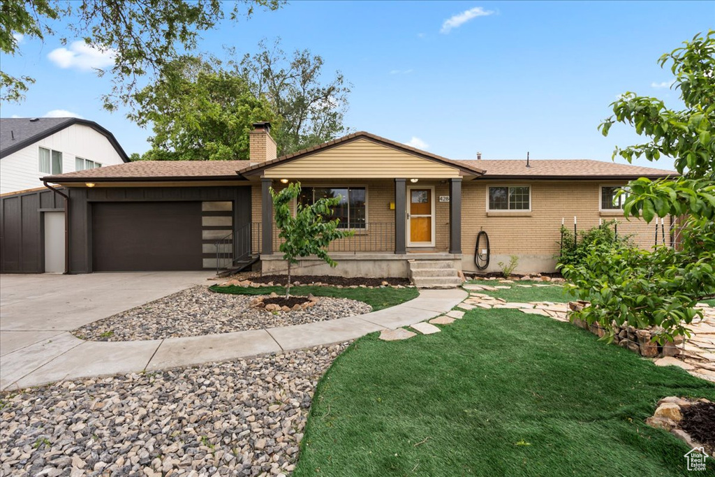 View of front of property featuring an attached garage, concrete driveway, brick siding, a chimney, and a front yard