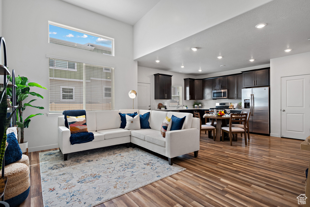 Living room with plenty of natural light, wood finished floors, a towering ceiling, recessed lighting, and baseboards