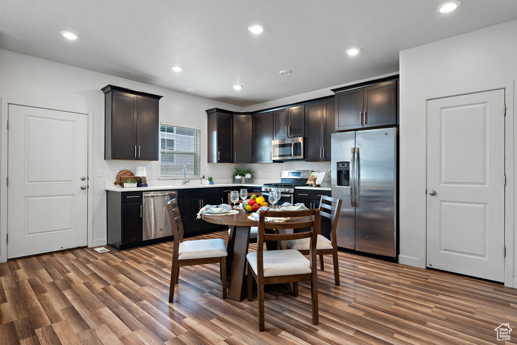 Kitchen with stainless steel appliances, wood finished floors, light countertops, recessed lighting, and dark brown cabinets