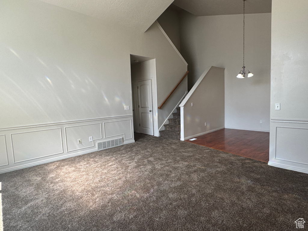 Unfurnished living room with carpet, stairway, vaulted ceiling, and a decorative wall