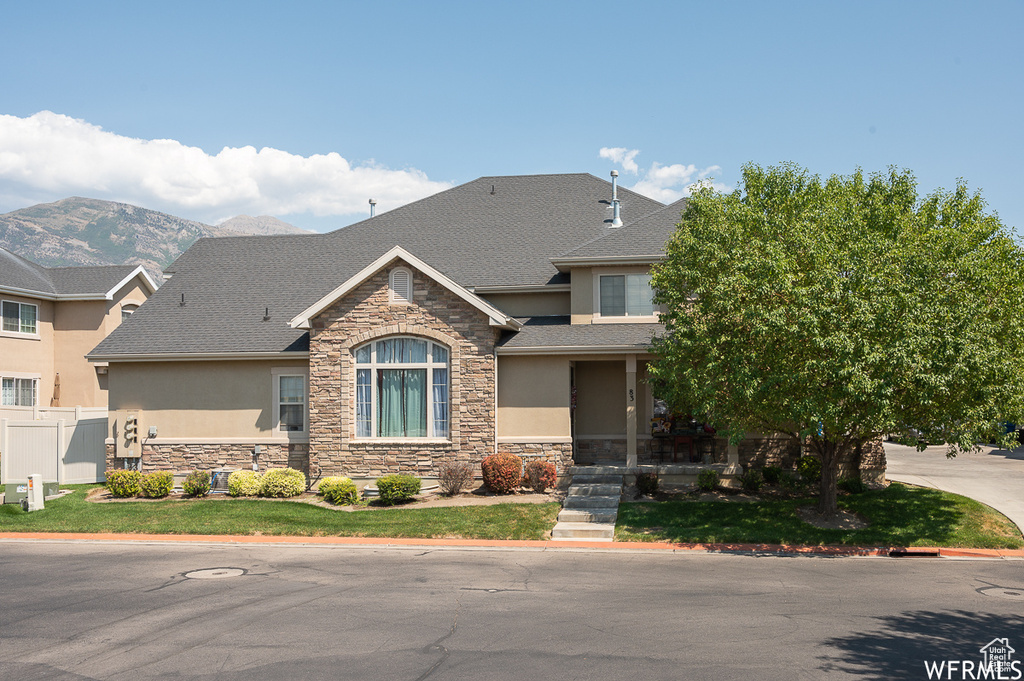 View of front of property with stucco siding, stone siding, a shingled roof, and fence