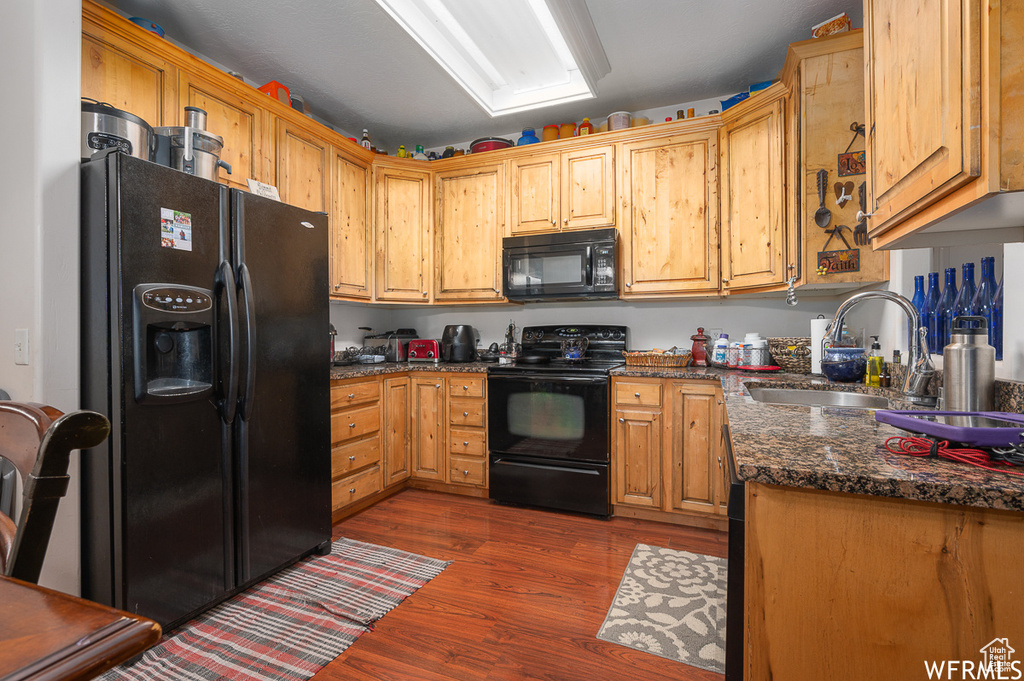 Kitchen with black appliances, a sink, dark wood-type flooring, and dark stone countertops