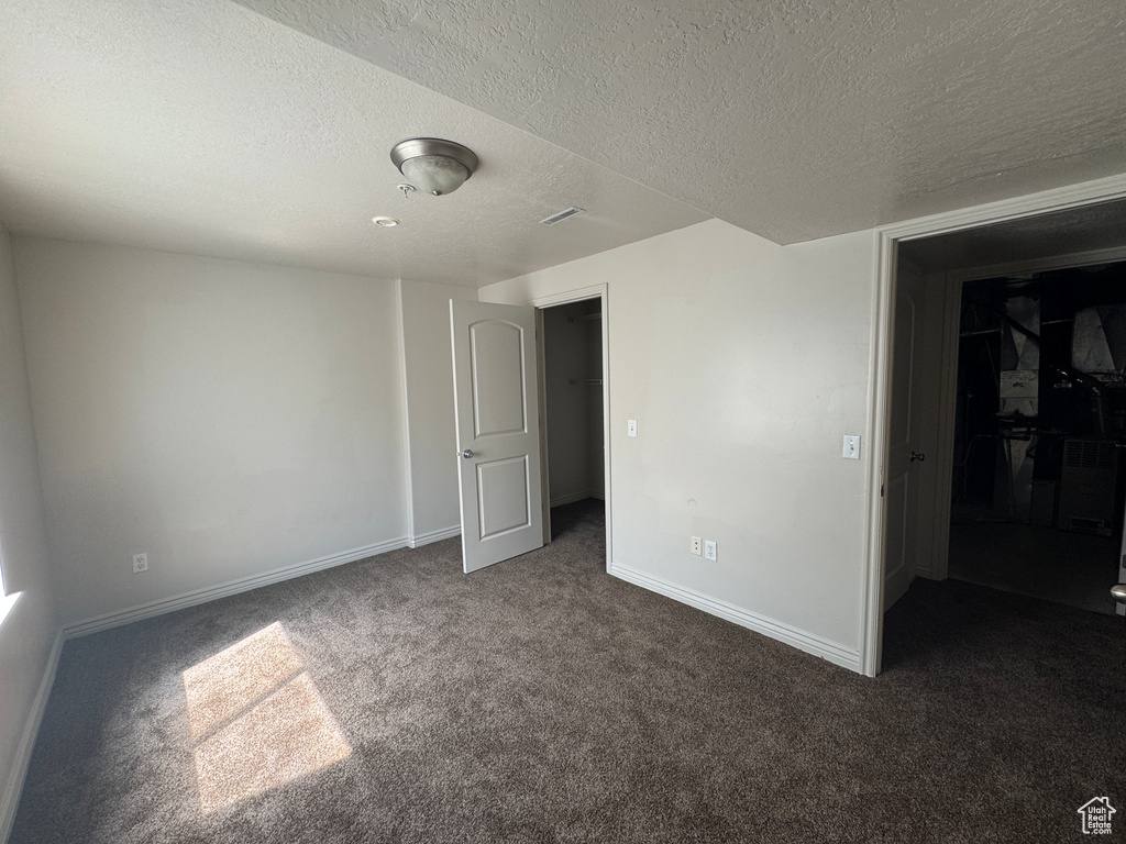Spare room with a textured ceiling, dark colored carpet, and baseboards