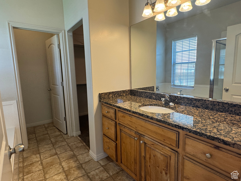 Full bathroom featuring vanity, a shower stall, a walk in closet, stone finish flooring, and baseboards
