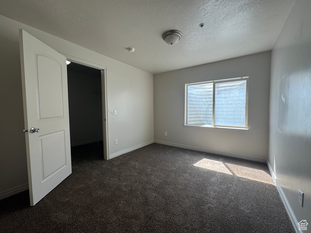 Unfurnished bedroom featuring dark carpet, a textured ceiling, and baseboards
