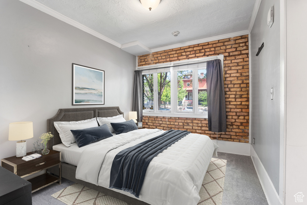 Carpeted bedroom with brick wall, a textured ceiling, ornamental molding, and baseboards