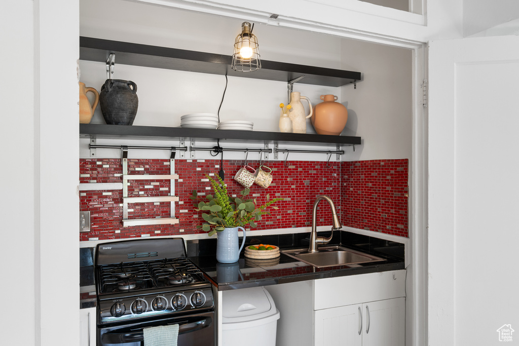 Kitchen featuring gas stove, a sink, open shelves, dark countertops, and white cabinets
