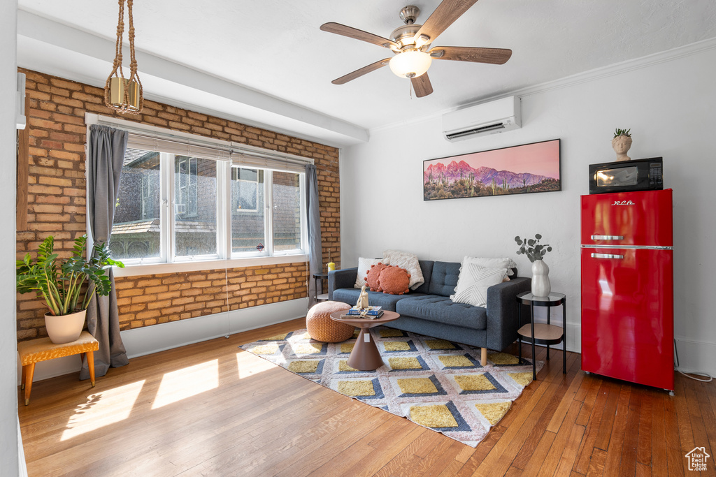 Living area featuring a wall mounted air conditioner, hardwood / wood-style floors, a ceiling fan, brick wall, and baseboards