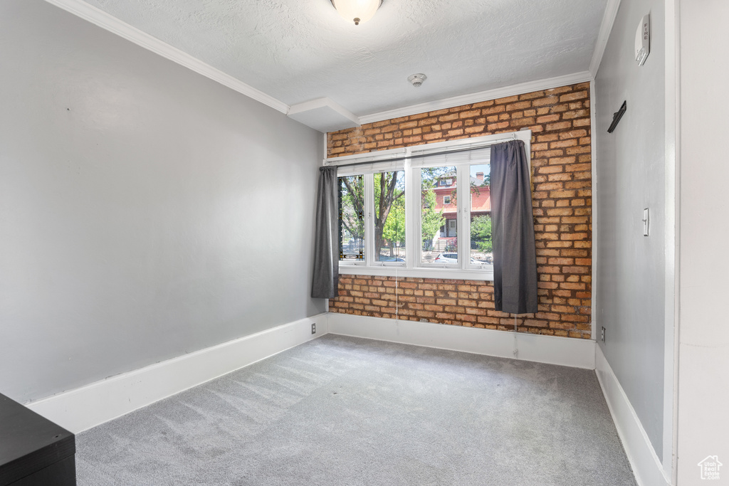 Carpeted spare room featuring a textured ceiling, crown molding, brick wall, and baseboards