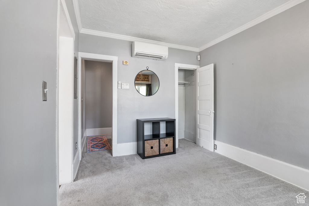 Unfurnished bedroom with a wall mounted air conditioner, carpet flooring, a textured ceiling, ornamental molding, and baseboards