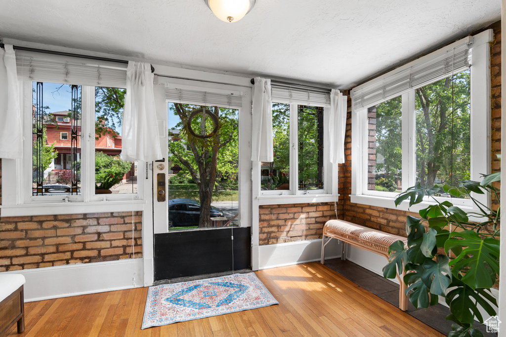 Sunroom featuring healthy amount of natural light, wood finished floors, brick wall, and baseboards