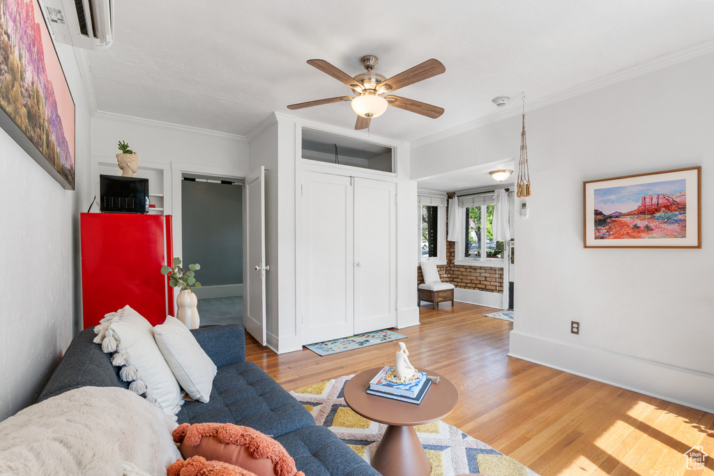 Living area featuring light wood-style flooring, a ceiling fan, baseboards, ornamental molding, and an AC wall unit