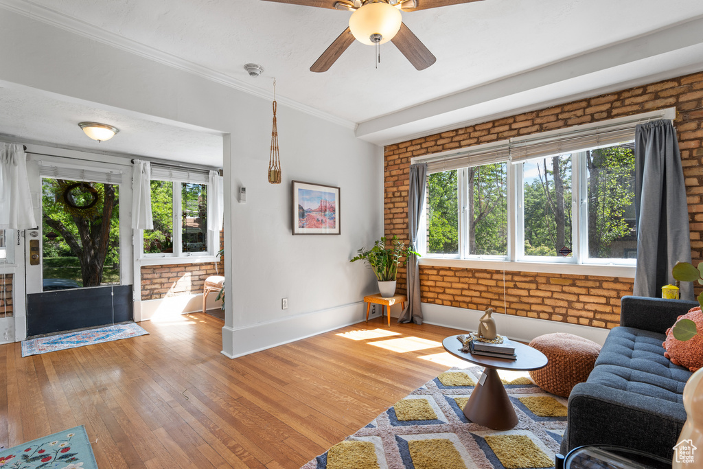 Living area featuring brick wall, light wood-type flooring, a ceiling fan, baseboards, and crown molding
