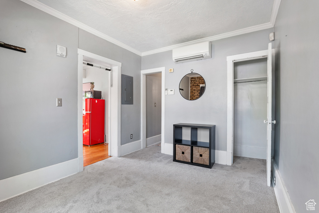 Unfurnished bedroom with a wall mounted air conditioner, carpet flooring, crown molding, electric panel, and a closet