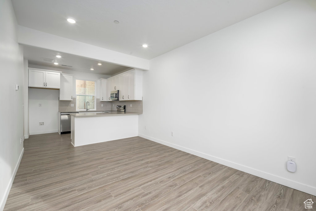Kitchen featuring appliances with stainless steel finishes, light wood finished floors, white cabinetry, a peninsula, and baseboards