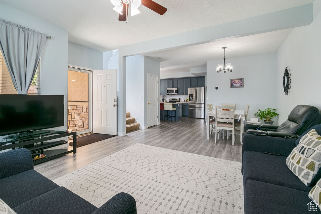 Living area featuring a chandelier, a ceiling fan, stairs, and light wood-type flooring