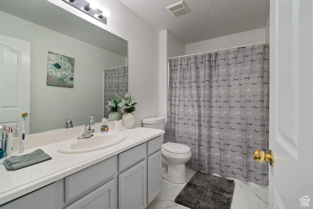 Bathroom with marble look tile flooring, vanity, toilet, a textured ceiling, and curtained shower