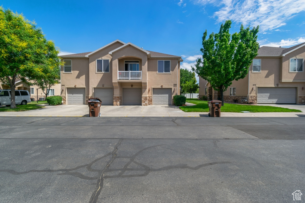 View of property with stucco siding, stone siding, an attached garage, and driveway