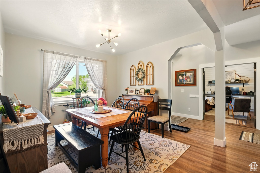 Dining area with arched walkways, light wood-style floors, a chandelier, baseboards, and a desk