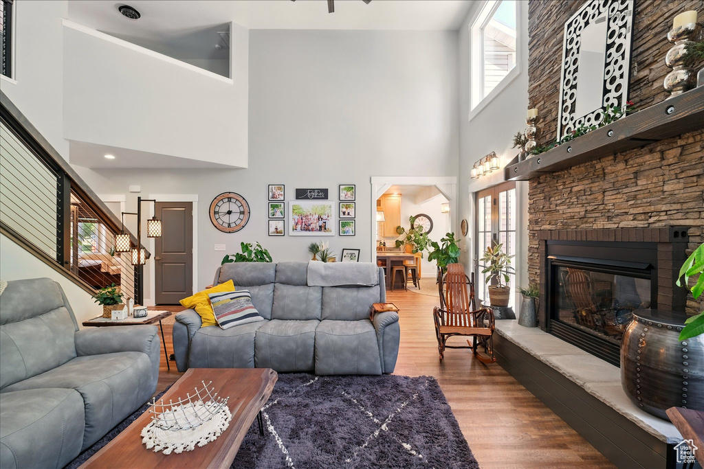 Living room featuring a high ceiling, wood finished floors, a stone fireplace, and stairway