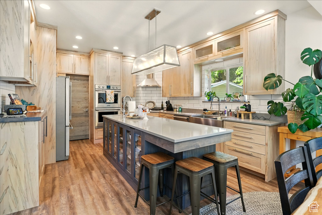 Kitchen featuring a sink, appliances with stainless steel finishes, light brown cabinets, a breakfast bar, and an island with sink