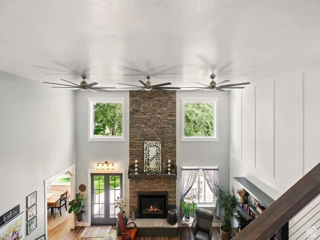 Living room featuring a fireplace, healthy amount of natural light, wood finished floors, a towering ceiling, and a ceiling fan