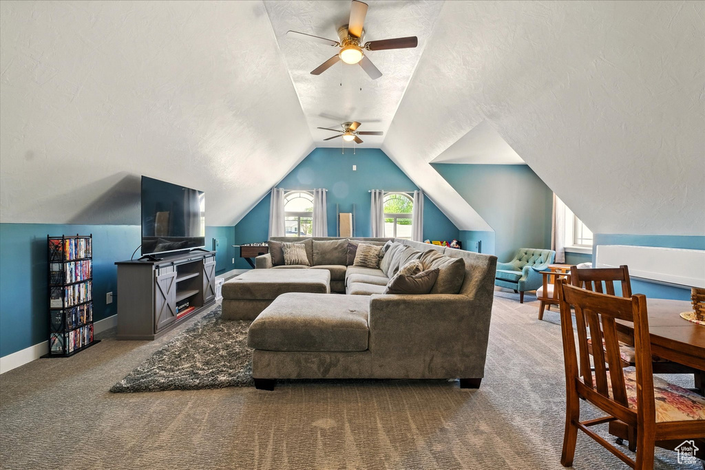 Carpeted living area with a ceiling fan, vaulted ceiling, baseboards, and a textured ceiling