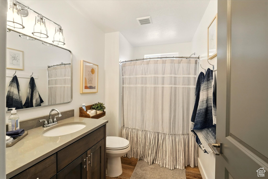 Bathroom with wood finished floors, vanity, toilet, and a shower with curtain