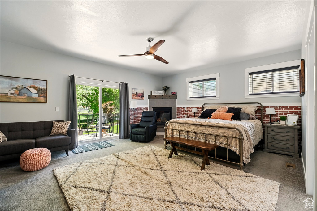 Carpeted bedroom with access to exterior, multiple windows, a tiled fireplace, and a ceiling fan