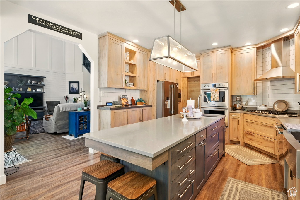 Kitchen with appliances with stainless steel finishes, wall chimney range hood, light brown cabinetry, open shelves, and recessed lighting