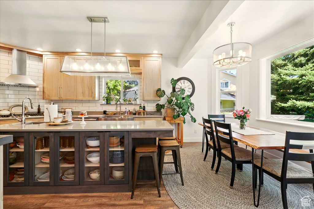 Kitchen with wall chimney exhaust hood, light brown cabinets, wood finished floors, backsplash, and a chandelier