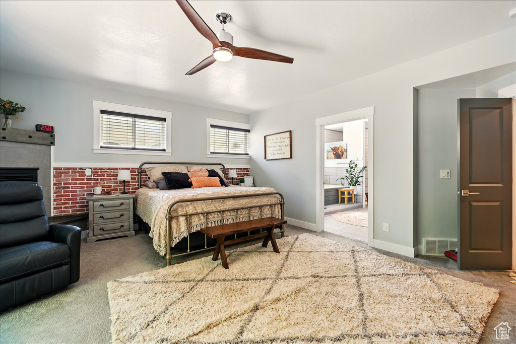 Carpeted bedroom featuring ensuite bath, a tile fireplace, and ceiling fan