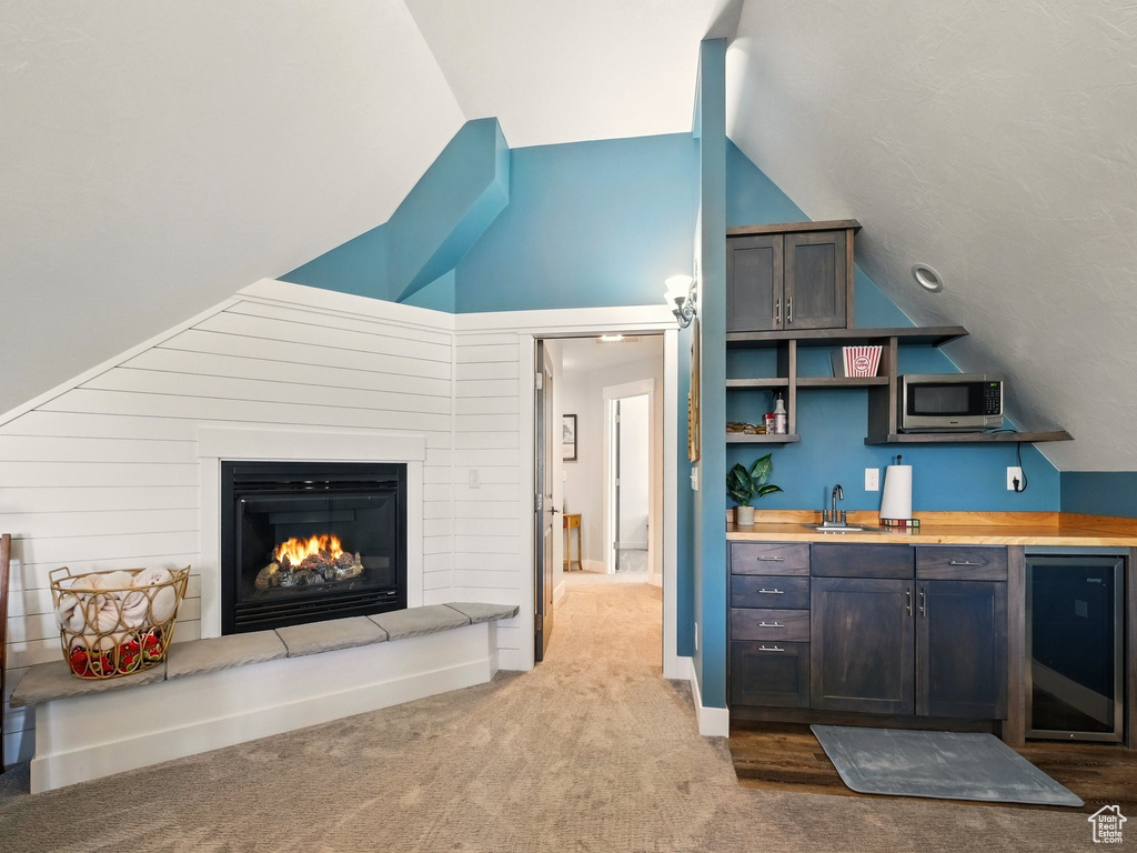 Kitchen with stainless steel microwave, vaulted ceiling, a sink, carpet flooring, and a glass covered fireplace