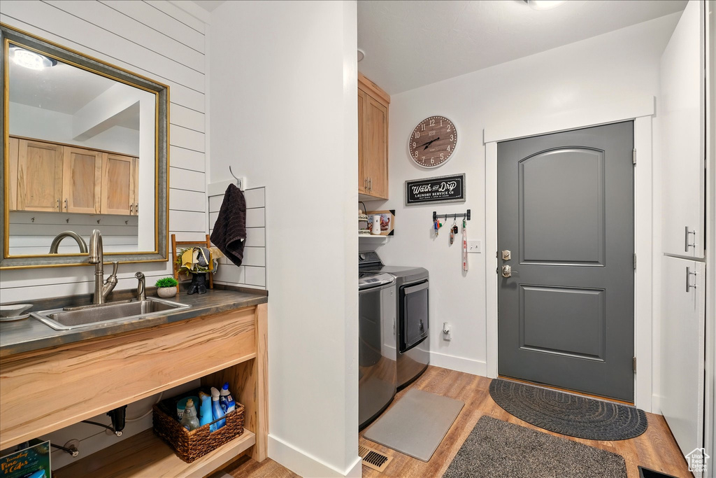 Kitchen with separate washer and dryer, a sink, light wood-style flooring, stainless steel countertops, and baseboards