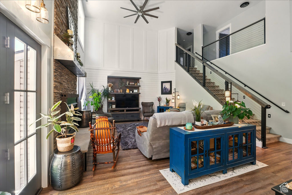 Living area with stairway, wood finished floors, ceiling fan, a towering ceiling, and a fireplace
