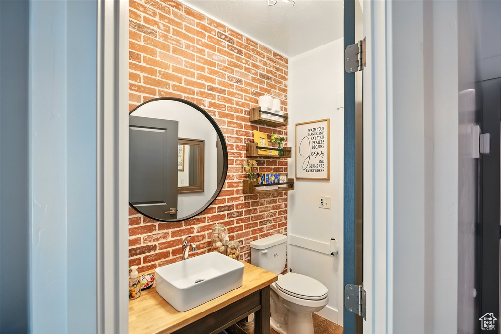 Half bathroom with a sink, brick wall, and toilet