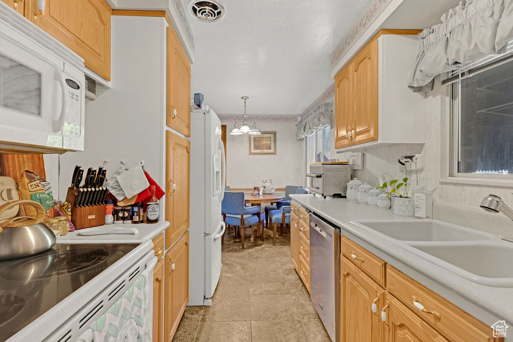 Kitchen with white appliances, light countertops, a sink, and pendant lighting