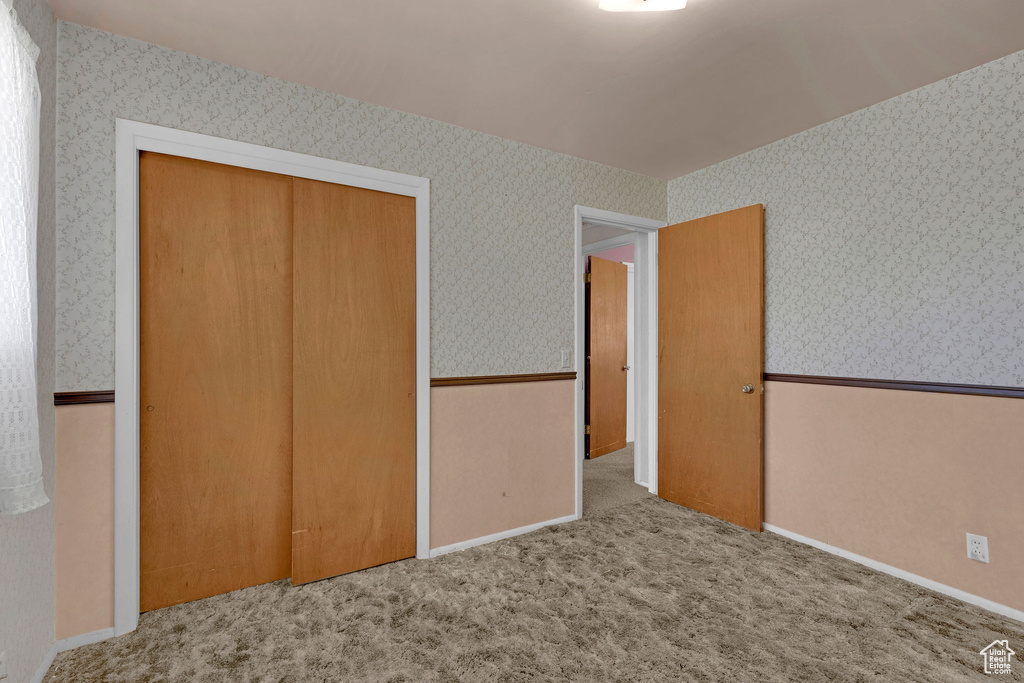 Unfurnished bedroom featuring wallpapered walls, a closet, and carpet flooring