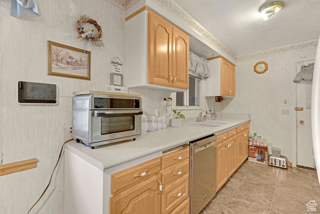 Kitchen featuring dishwasher, a sink, light countertops, and wallpapered walls