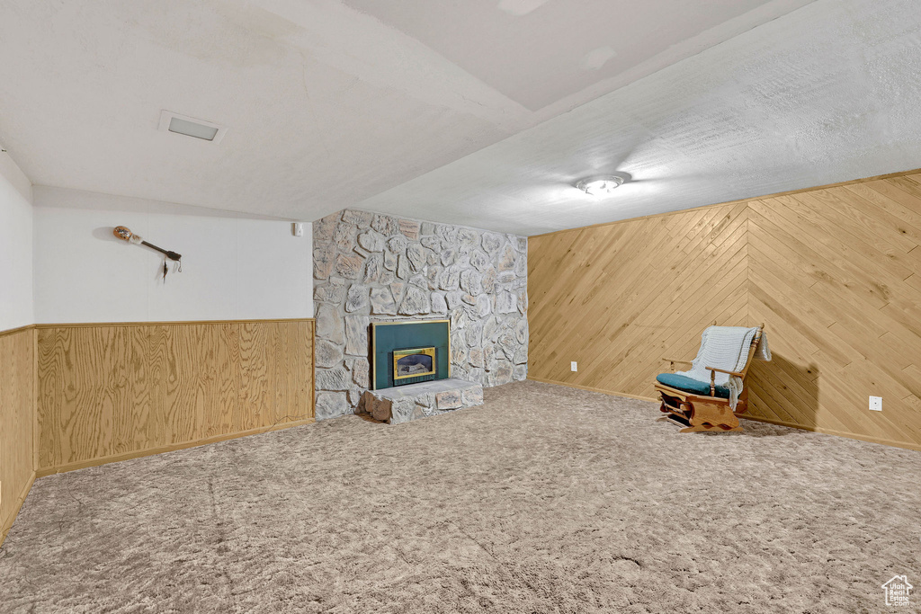 Unfurnished living room with wooden walls, a fireplace, carpet flooring, and a wainscoted wall