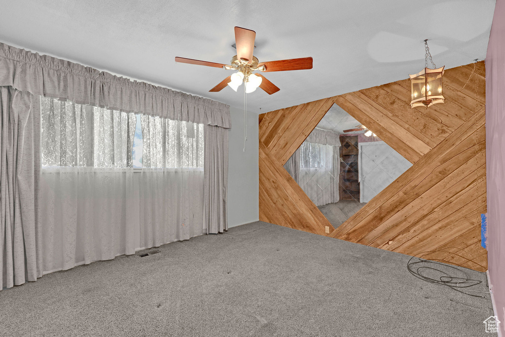 Carpeted spare room featuring wood walls and ceiling fan